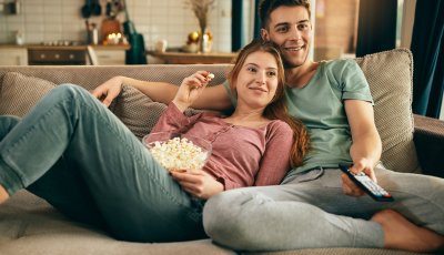 Young happy couple relaxing while watching TV and eating popcorn at home.