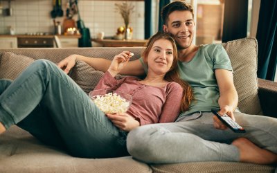 Young happy couple relaxing while watching TV and eating popcorn at home.