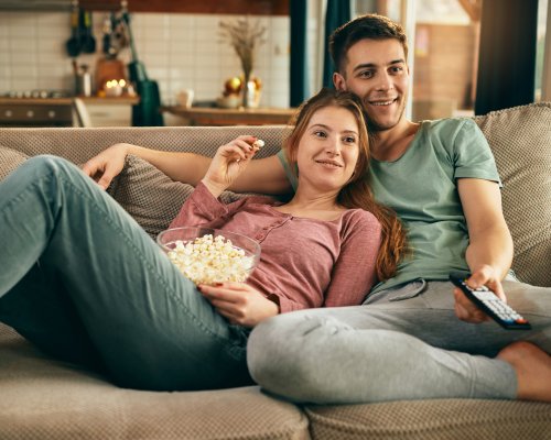 Young happy couple relaxing while watching TV and eating popcorn at home.