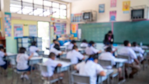 Education evaluation, Blurred image of Writing test in exam with behind child asian students group concentrate in primary school, final examination desk at classroom with Thai student uniform.